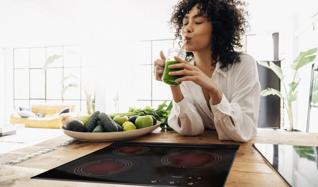 Young african american woman drinking green juice with reusable bamboo straw in loft apartment. Copy space