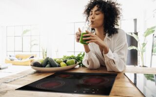 Young african american woman drinking green juice with reusable bamboo straw in loft apartment. Copy space