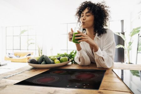 Young african american woman drinking green juice with reusable bamboo straw in loft apartment. Copy space